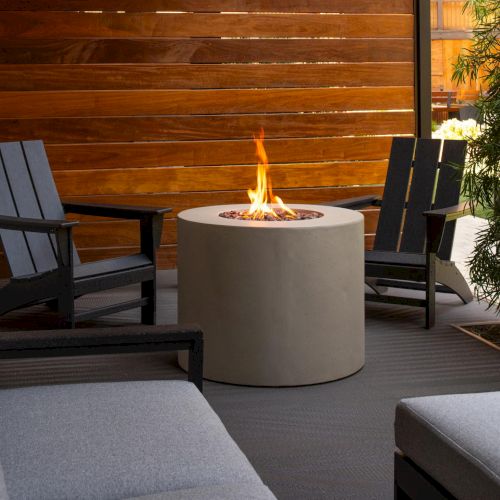 A cozy outdoor seating area with a built-in fire pit, concrete round table, and cushioned lounge chairs around a warm flame.